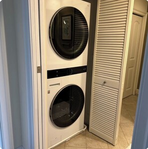 A compact, wall-mounted washer and dryer unit in a hallway with a door leading to another room.
