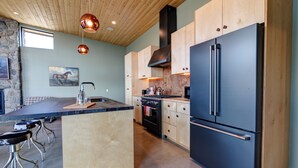 Cocina moderna con una isla central, estufa, refrigerador e iluminación colgante.