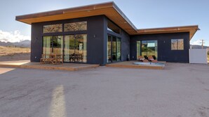 Un edificio moderno con grandes ventanales de vidrio, una terraza de madera y una zona de piscina.