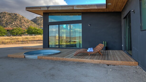 Un edificio moderno con terraza de madera, jacuzzi y una tumbona.