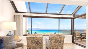 Ett rum med ett stort fönster med utsikt över en strand, en soffa, två fåtöljer, ett soffbord i trä och en lampa.