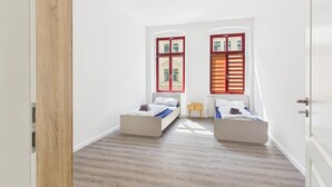 Quarto com duas camas, porta de madeira e janela com persianas.