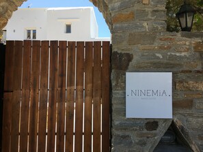 Ein hölzernes Tor, eine Steinmauer und ein Schild mit der Aufschrift 'NINEMIA NAXOS SUITES'.