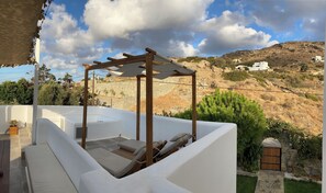 Eine Dachterrasse mit einer Holz-Pergola, weißen Liegestühlen und Blick auf eine hügelige Landschaft mit Gebäuden.