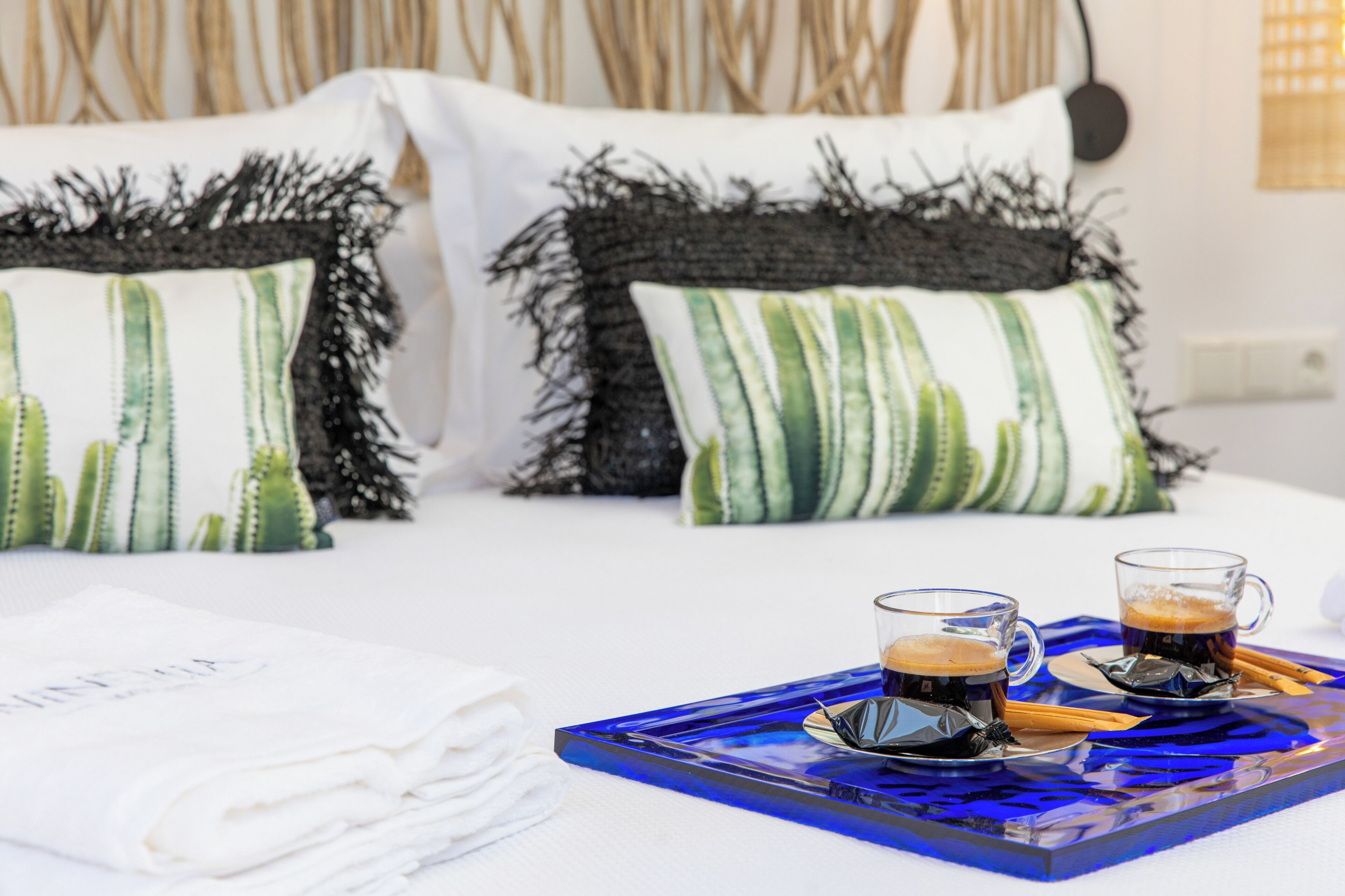 Un lit bien fait avec deux oreillers, un plateau bleu sur lequel reposent deux tasses de café et une serviette blanche.