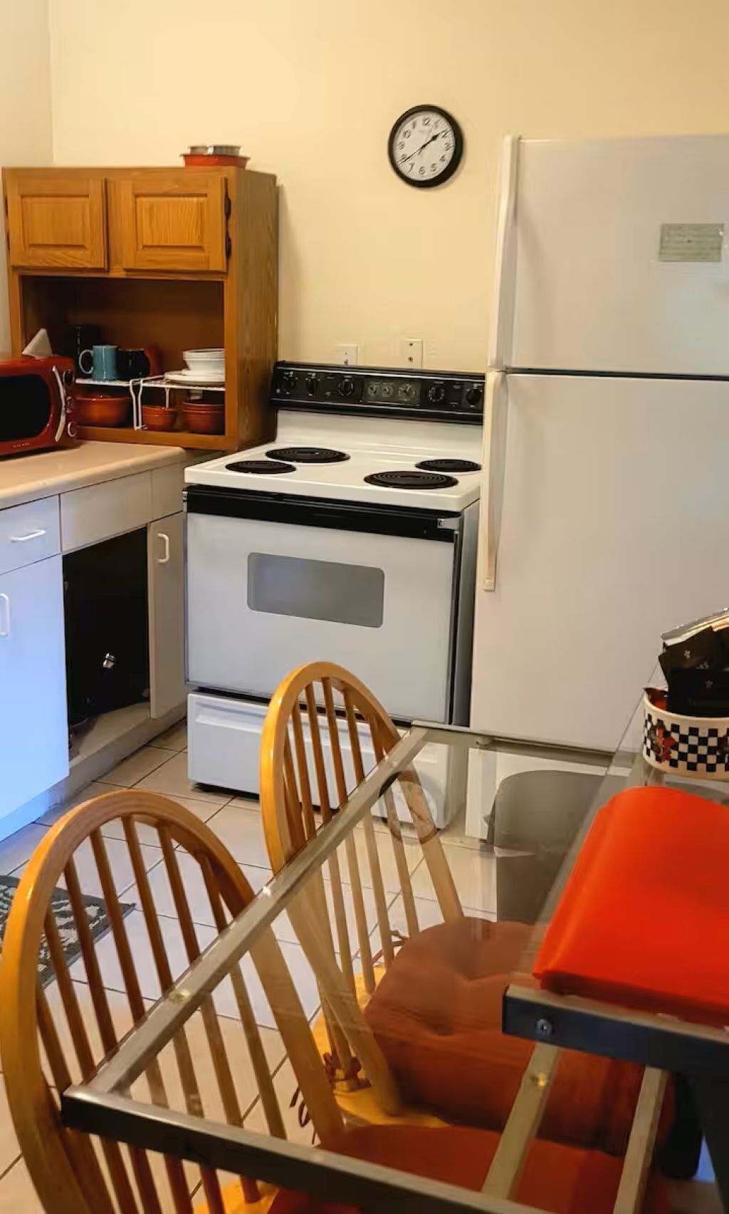 A kitchen with a stove, refrigerator, wooden cabinets, and a clock on the wall.