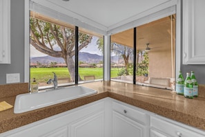 A kitchen with a large window, a sink, and a countertop with bottles.