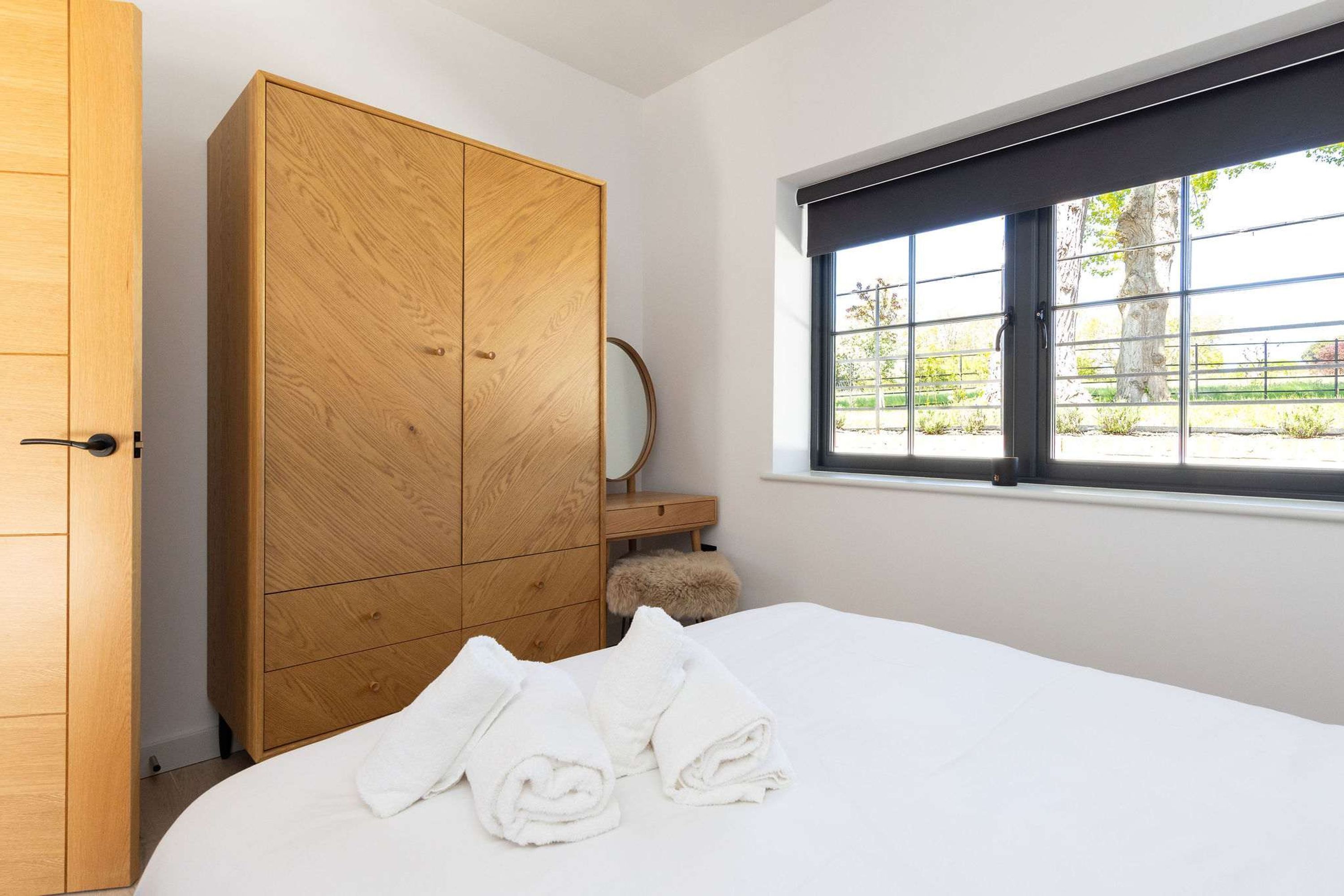A bedroom with a large wooden wardrobe, a bed with white linens, and a window with a view of greenery.