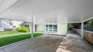Un patio cubierto con piso de concreto, cerca de madera y un arbusto verde.