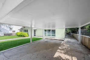 Un patio cubierto con piso de concreto, cerca de madera y un arbusto verde.