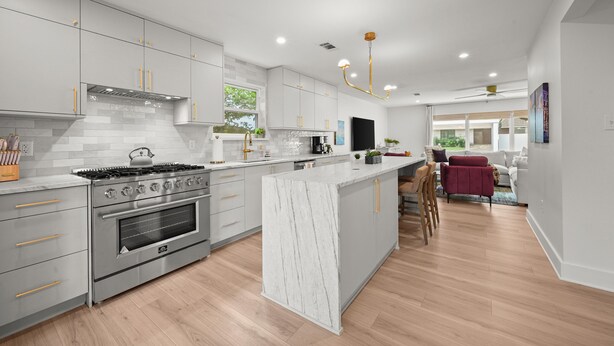 Una cocina moderna con una isla central, electrodomésticos de acero inoxidable y un comedor con una silla roja y un sofá.