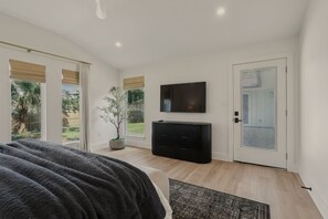 Una camera da letto con un letto grande, una televisione, una pianta in vaso e una porta che dà su un balcone.