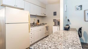 Una cocina con armarios blancos, encimera de granito, refrigerador, estufa y pileta.