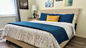 Un dormitorio con cama, mesita de noche, lámpara y ventana con persianas.