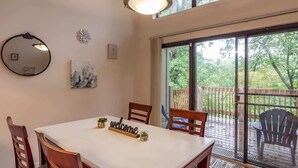 Un coin repas comprenant une table, des chaises, une pancarte « Bienvenue », un miroir et une vue sur une terrasse extérieure, accessible par une porte vitrée.