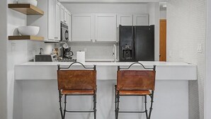 A modern kitchen with white cabinets, a black refrigerator, and two leather chairs. - Riverfront Ski & Fish Condo, Near BC & Vail (Edwards)