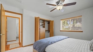 Ein Schlafzimmer mit Bett, Deckenventilator, Kleiderschrank, Fenster mit Jalousien und Tür.