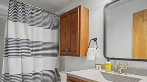 Ein Badezimmer mit gestreifter Duschvorhang, Toilette, Holzschränken, Waschbecken mit Spiegel und Handtuchhalter.