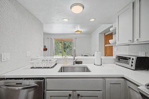 A modern kitchen with white cabinetry, a built-in oven, a sink, and a window with a view of greenery. - Eagle River Ski & Fish, Shuttle, Near BC & Vail (Edwards)