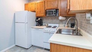 A compact kitchen with wooden cabinets, a white refrigerator, a microwave, a stove, and a sink. - Woodland Escape Condo (Bloomington)