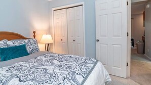 A bedroom with a bed, a nightstand, a lamp, and two white doors. - Woodland Escape Condo (Bloomington)