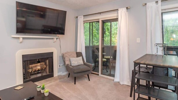 A living room with a fireplace, a television, a dining table, and a sliding glass door to the outside. - Woodland Escape Condo (Bloomington)