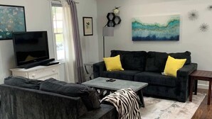A living room with a sofa, a coffee table, a TV, and a painting on the wall.