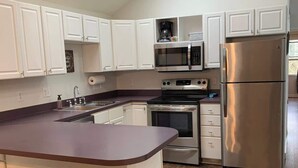A kitchen with white cabinets, a stainless steel refrigerator, a microwave, and an oven. There are two stools at the island.