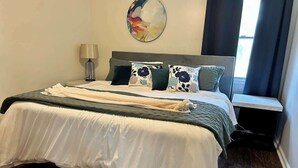 A neatly made bed with a white and grey duvet, a bedside lamp, and a round wall decoration.