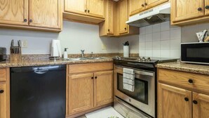 A kitchen with wooden cabinets, a dishwasher, an oven, a microwave, and a granite countertop. - Convenient Wayfarer’s Rest (Bloomington)