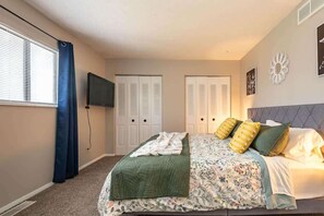 A bedroom with a bed, a TV, two doors, and a window with curtains.