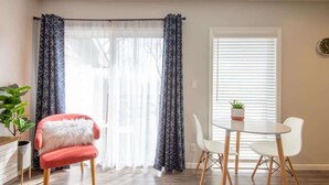 Un coin repas avec une table et des chaises, une chaise rouge avec un coussin blanc, et une plante en pot posée sur la table.