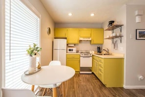 Une cuisine de taille réduite avec des meubles de couleur jaune, un réfrigérateur blanc, un four à micro-ondes, une cuisinière et un évier.
