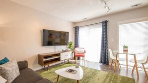 Un salon moderne comprenant un canapé, une table basse, un téléviseur et un coin repas avec des chaises et une table.