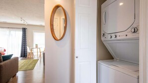Une buanderie avec un lave-linge blanc, un miroir à cadre en bois et une porte donnant sur une autre pièce.
