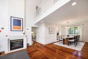 A spacious living area with hardwood flooring, a fireplace, a dining table with chairs, and a staircase leading to an upper level. - Spacious 4BR Kirkland Retreat, Games (Kirkland)