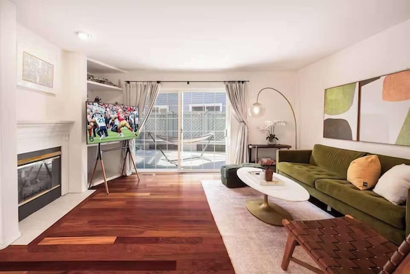 A living room with a green sofa, a coffee table, a fireplace, a TV, and a large window with curtains. - Spacious 4BR Kirkland Retreat, Games (Kirkland)