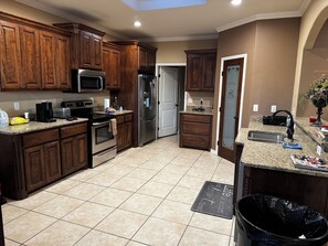A kitchen with wooden cabinets, stainless steel appliances, a granite countertop, and a black trash bin. - Spacious 4-bedroom house in Midland with AC (Midland)