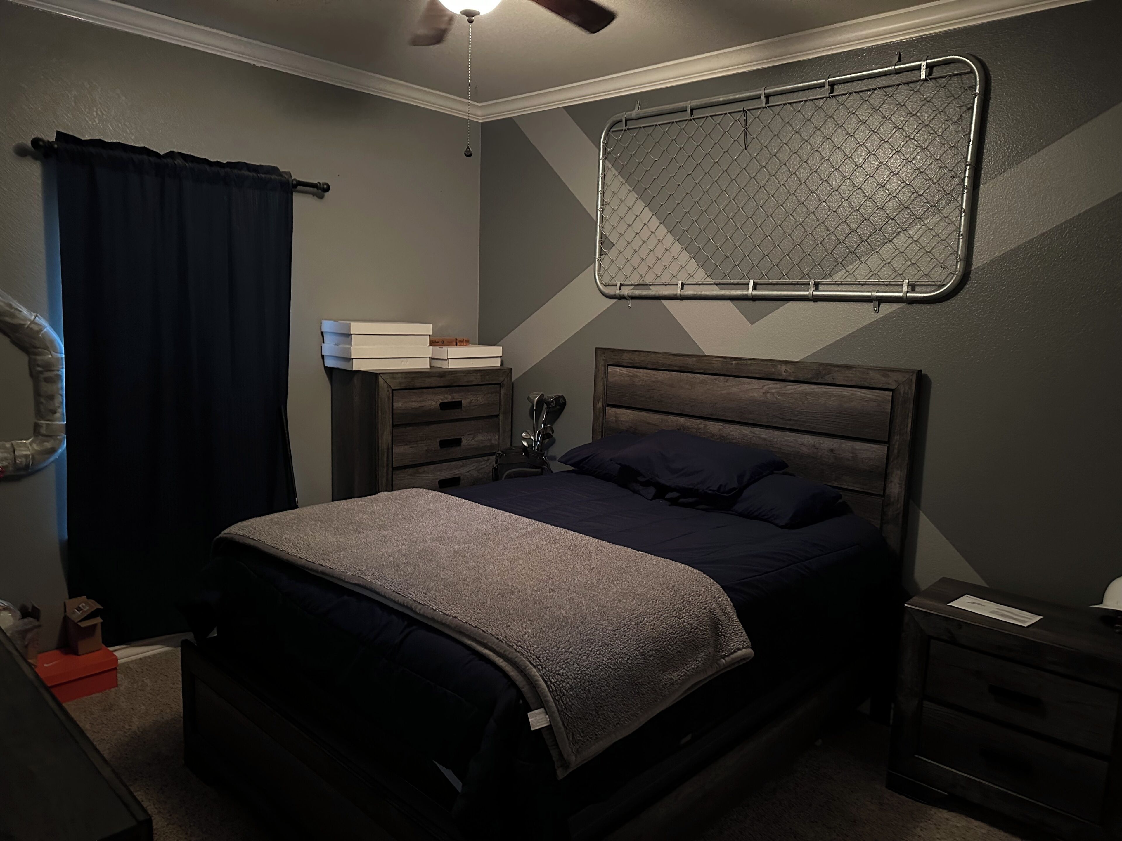 A bedroom with a bed, a dresser, a nightstand, a ceiling fan, and a window with curtains.