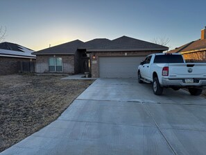 A residential driveway with a white pickup truck parked in front of a house with a garage. - Spacious 4-bedroom house in Midland with AC (Midland)