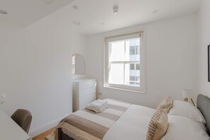 Ein Schlafzimmer mit einem Bett, einem Schminktisch, einem Fenster und einem Schreibtisch.
