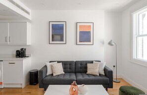 Ein modernes Wohnzimmer mit einem grauen Sofa, zwei gerahmten Kunstwerken, einer Kaffeemaschine und einer Stehlampe.