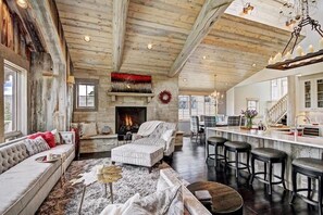A spacious living room with a fireplace, a bar area, and a large window. - Luxury Mountain Estate wHot Tub Sauna & Movie Room (Breckenridge)
