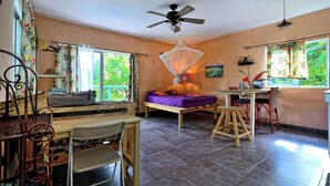 Una habitación con cama, una mesa, una silla, ventilador de techo y ventana con cortinas.