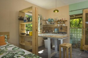 Une pièce compacte comprenant un lit, une petite kitchenette et une fenêtre donnant sur un espace verdoyant.