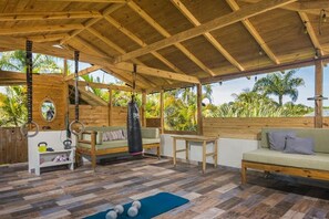 Un espace extérieur abrité, doté d’un plafond en bois, d’équipements de musculation, d’un canapé et d’une table.