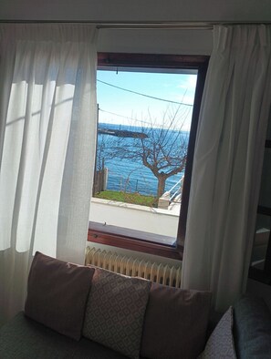 Ein Zimmer mit Meerblick durch ein Fenster mit weißen Vorhängen.