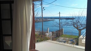 Vista desde una ventana con cortina, con vista a un cuerpo de agua, un muelle y un árbol.