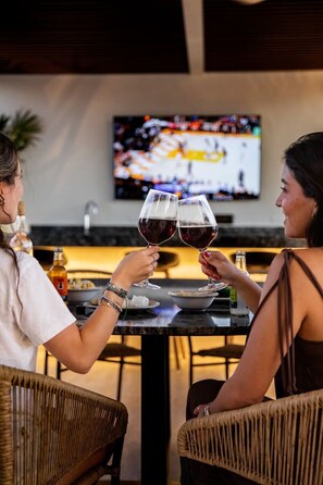 Two people toasting with wine glasses at a bar with a television in the background. - Casa del Paseo| Rooftop Bar + 2 Pools near Montejo (Mérida)