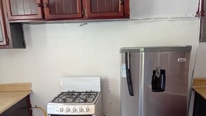Una cocina con estufa blanca, refrigerador de acero inoxidable, gabinetes de madera y piso de baldosas.
